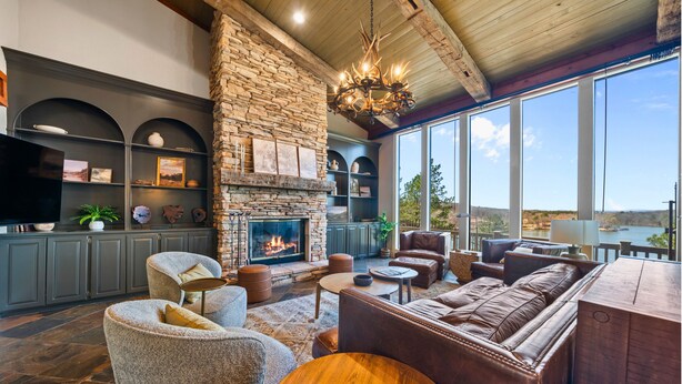 A spacious living room with a stone fireplace, leather sofas, and a large window overlooking a scenic view. - One Acre Private Oasis, Saltwater Pool, New Sauna, Outdoor Kitchen, and Fire Pit (Hot Springs)