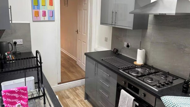 A modern kitchen with a gas stove, black cabinets, and a stainless steel range hood. - 2 Bed - Sleeps 4 - Garden - Free Parking (Wednesfield)