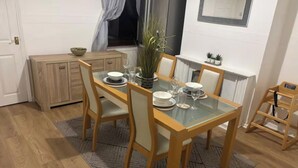 A dining area with a glass-top table, wooden chairs, and a small cabinet. - 2 Bed - Sleeps 4 - Garden - Free Parking (Wednesfield)