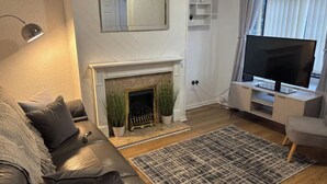 A living room with a fireplace, a sofa, a television, and a large window with blinds. - 2 Bed - Sleeps 4 - Garden - Free Parking (Wednesfield)