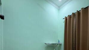 Quarto com piso de mármore, luminária no teto, janela com cortinas marrons e uma pequena mesa com um borrifador.