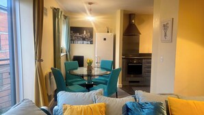 A modern living room with teal and yellow cushions, a round glass table with a vase, and a kitchen with a stainless steel range hood. - Peaceful Urban Retreat in Wolverhampton city (Wolverhampton)