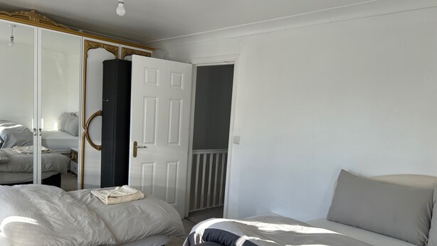 A bedroom with two beds, a wardrobe with a mirror, and a door leading to a balcony. - Romford Contractor / Family House (Romford)