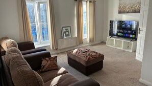 A living room with a sofa, ottoman, and a TV on a stand. - Romford Contractor / Family House (Romford)