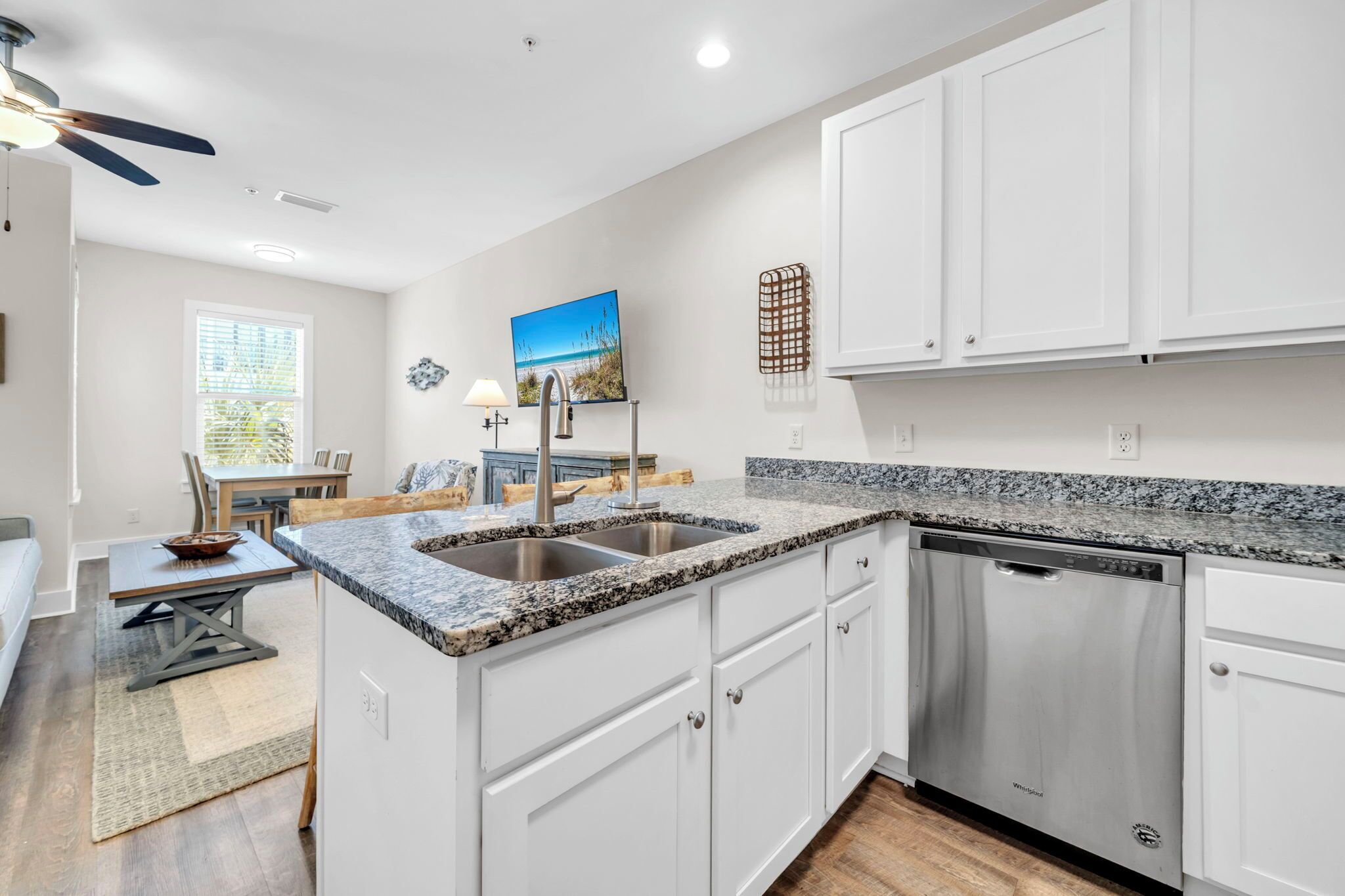 A modern kitchen with white cabinets, granite countertops, and a built-in dishwasher.