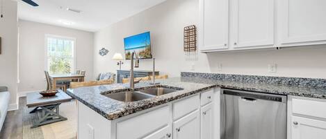 A modern kitchen with white cabinets, granite countertops, and a built-in dishwasher.