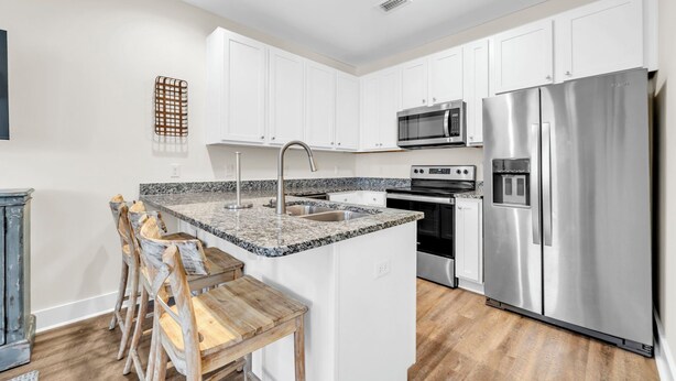 Una cocina moderna con armarios blancos, un refrigerador de acero inoxidable, horno empotrado y encimera de granito.