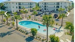 Un hotel con piscina, múltiples espacios de estacionamiento y una zona ajardinada con palmeras.