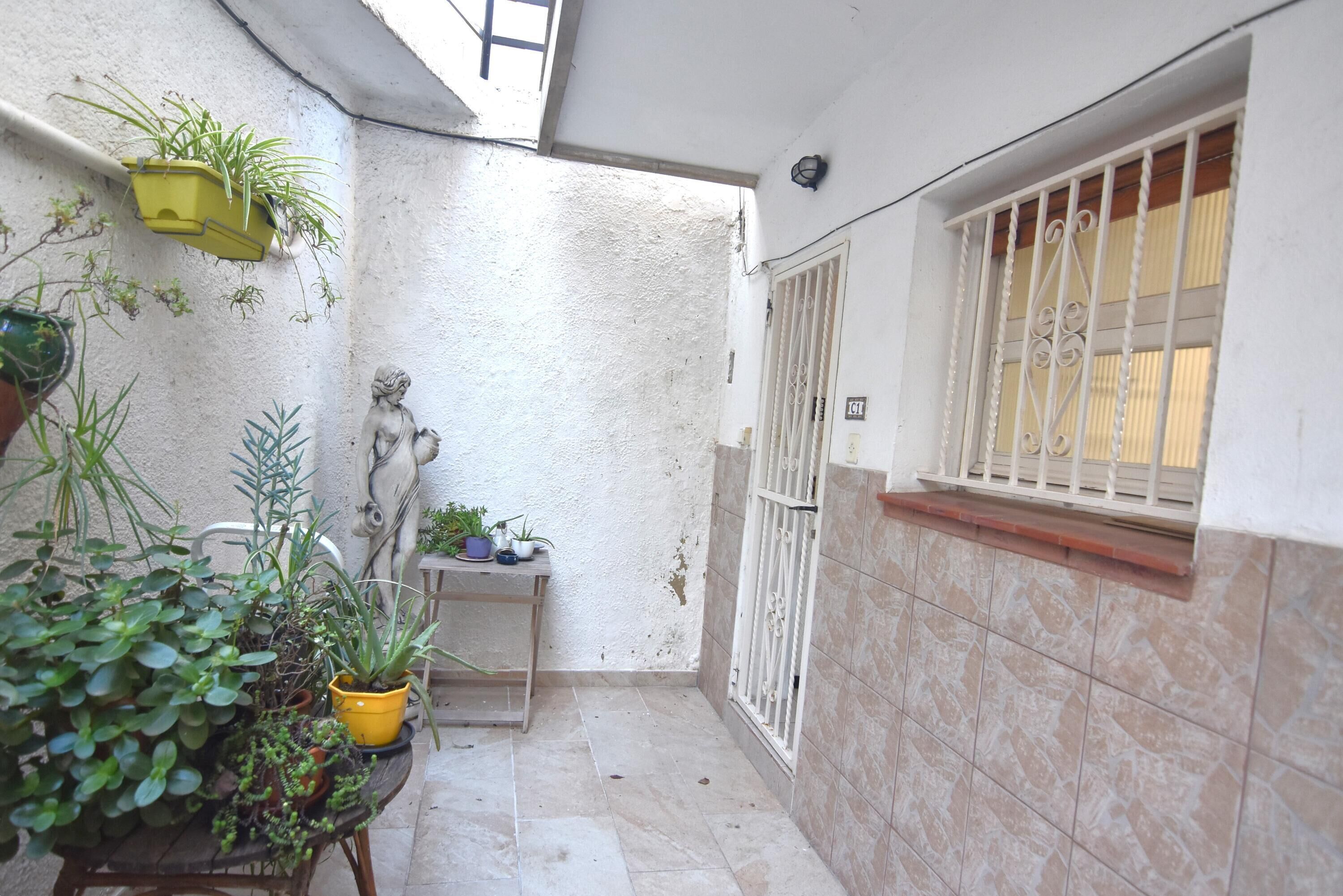 A small, enclosed outdoor area with potted plants, a statue, and a window with decorative bars.