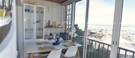 Un comedor con una mesa blanca, cuatro sillas blancas y vistas a la ciudad a través de amplios ventanales.