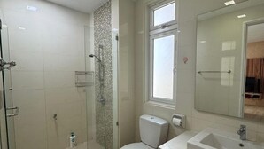 A modern bathroom with a glass-enclosed shower, a toilet, and a vanity with a sink. - Kuching Riverine Elegant Suite (Kuching)