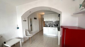 Eine kompakte Küche mit weißen Schränken, einem roten Kühlschrank und einer kleinen Essecke mit weißem Tisch und Stuhl.