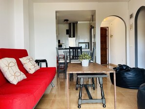 A modern living room with a red sofa, a dining table, and a black bean bag. - ROMINA. Spacious  Apartment in Roses – Quiet Area (Roses)