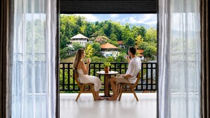 Un balcon donnant sur une végétation luxuriante et des maisons.