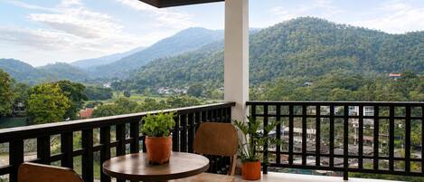 A balcony with a table and chairs, potted plants, and a view of a mountainous landscape.