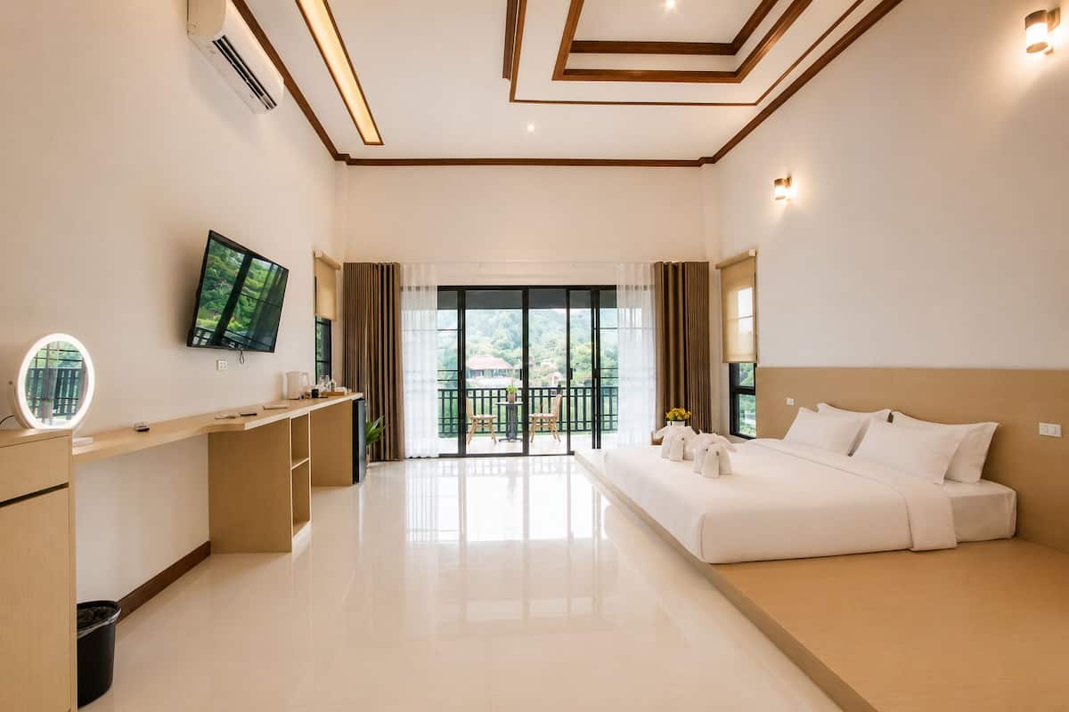 Een hotelkamer met een bed, een bureau met een televisie, een balkon met uitzicht en een plafond met inbouwverlichting.