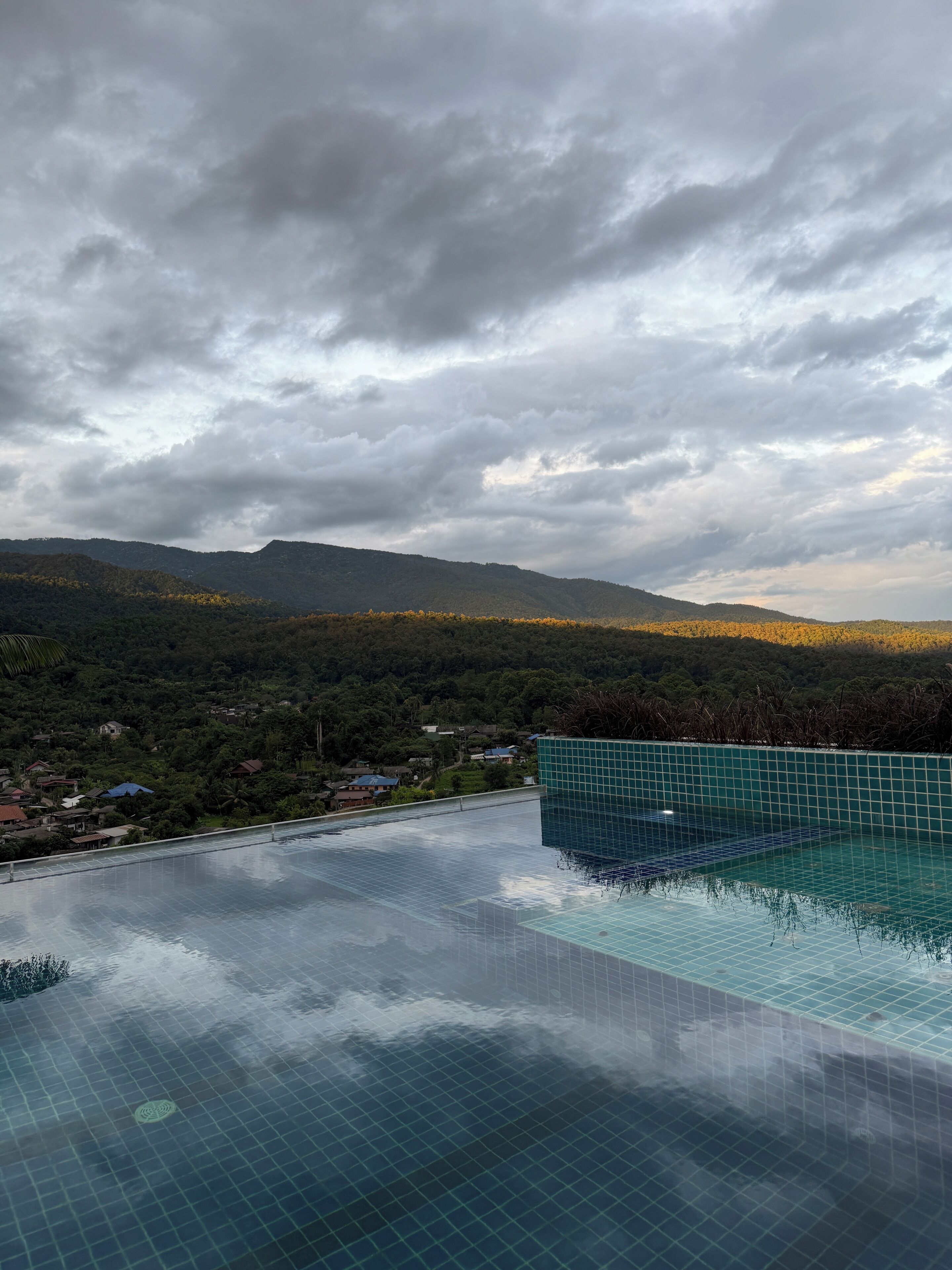 A rooftop infinity pool with a view of a forested hillside and distant mountains.