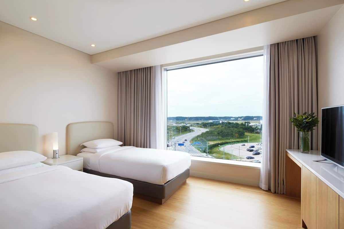 Habitación de hotel con dos camas, un ventanal con vistas a una autopista y un televisor de pantalla plana sobre un mueble de madera.
