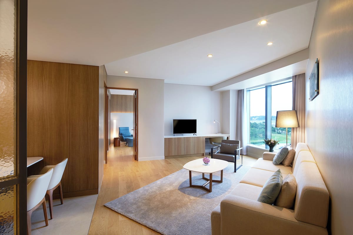 Una sala moderna con un sofá, una mesa de centro y un televisor. Cuenta con un comedor con sillas y una mesa. La habitación tiene ventanas amplias y vistas al exterior.