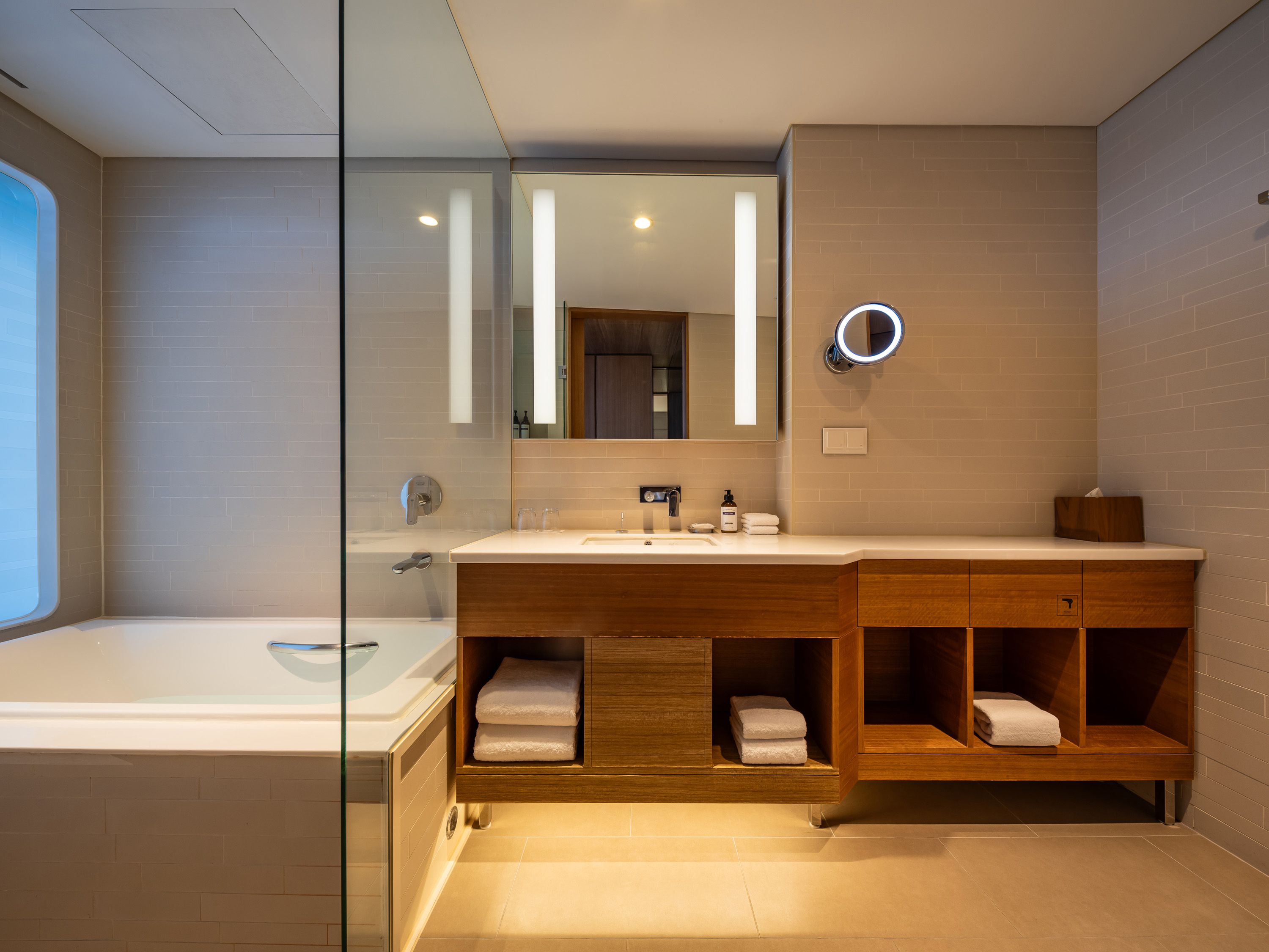 Une salle de bain moderne dotée d’une douche à parois de verre, d’un meuble-lavabo en bois avec un miroir et d’un porte-serviettes intégré.