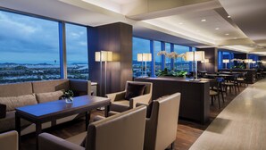 A modern hotel lobby with a large seating area, a bar, and large windows offering a city view.