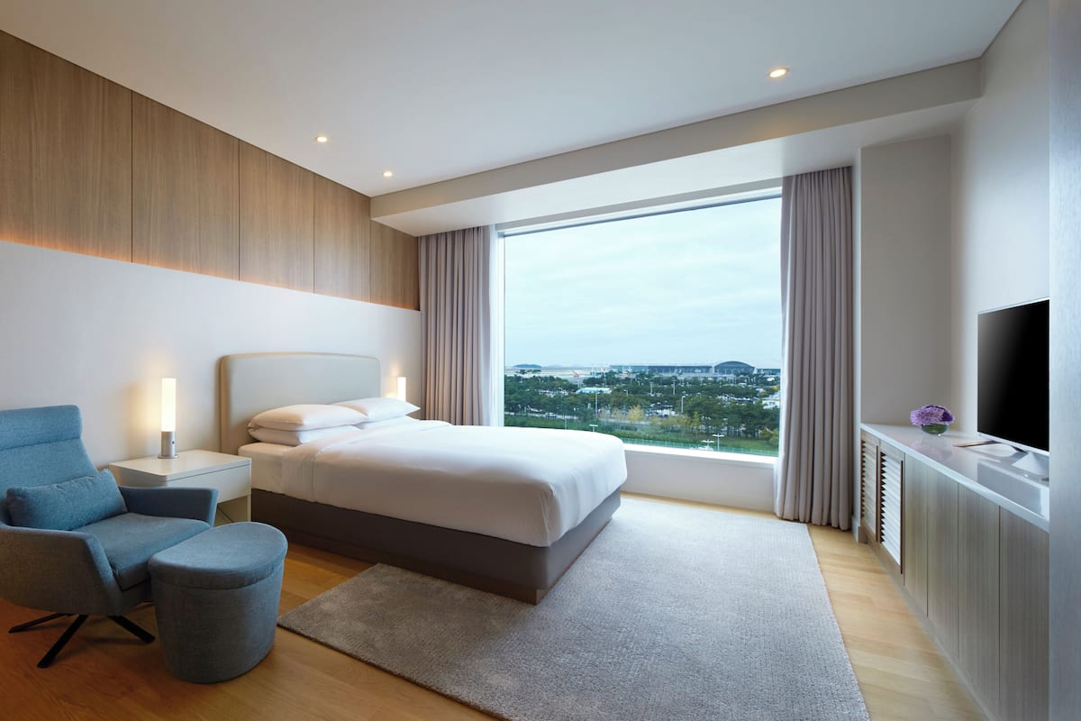 Una habitación de hotel moderna con una cama grande, zona de estar, televisor y vistas a la ciudad.