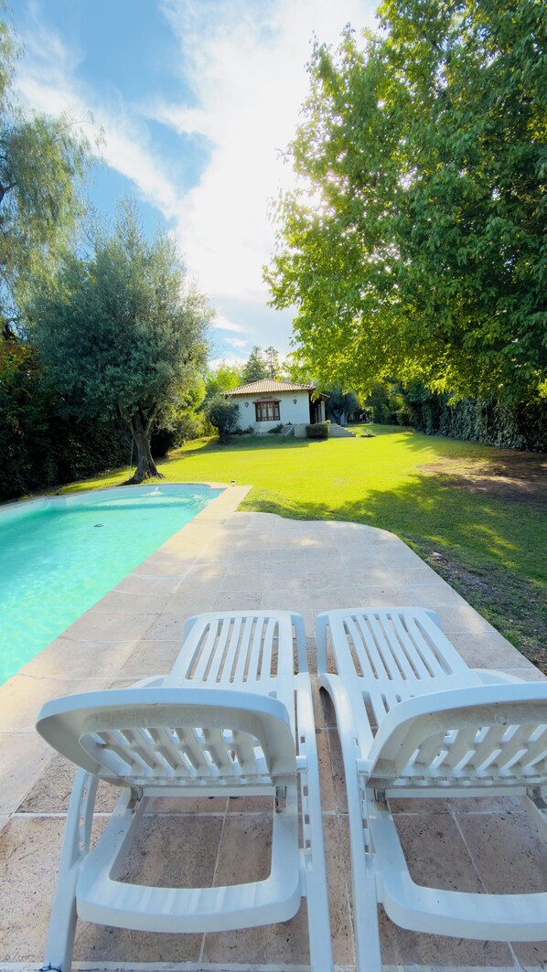 A swimming pool with two white lounge chairs facing it, surrounded by a well-maintained lawn and trees. - Quinta los caracoles de chacras (quiet and comfortable) (Luján de Cuyo)