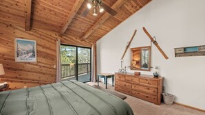 Quarto com cama, teto de madeira, cômoda, espelho e um esqui na parede.