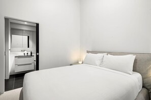 Quarto de hotel moderno com cama grande, roupeiro embutido e banheiro pequeno.