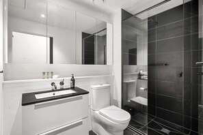 Uma casa de banho moderna com uma sanita, uma pia branca e zona de chuveiro com parede de vidro.