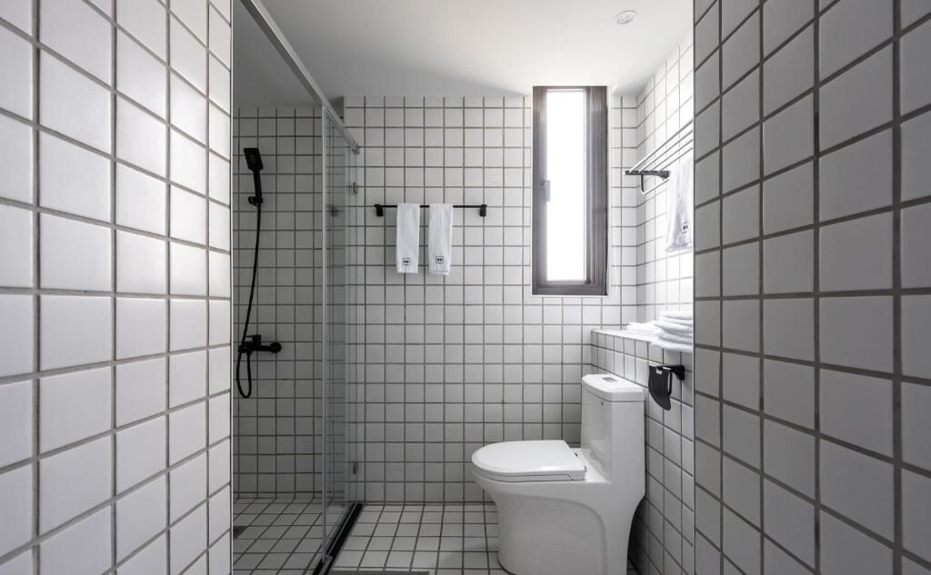 A modern bathroom with a shower, toilet, and a window.