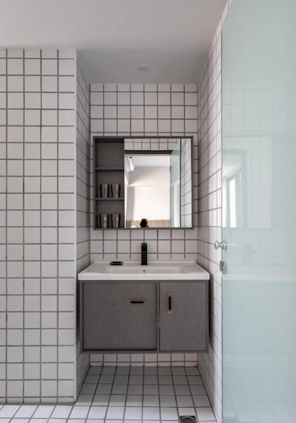 Un baño moderno con pared de azulejos, espejo, lavabo y armario.