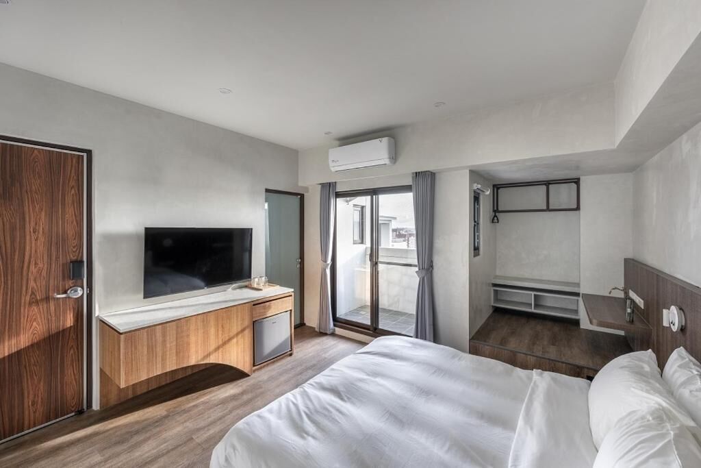 Ein modernes Hotelzimmer mit einem großen Bett, einem Fernseher, einem Holztisch und einem Balkon mit Blick.