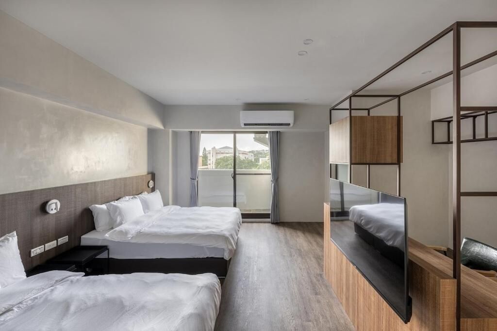 Quarto de hotel moderno com duas camas, uma janela grande e uma varanda.