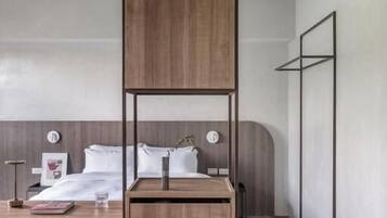 A modern hotel room with a bunk bed, a desk with a chair, a small refrigerator, and a bedside table with a lamp.