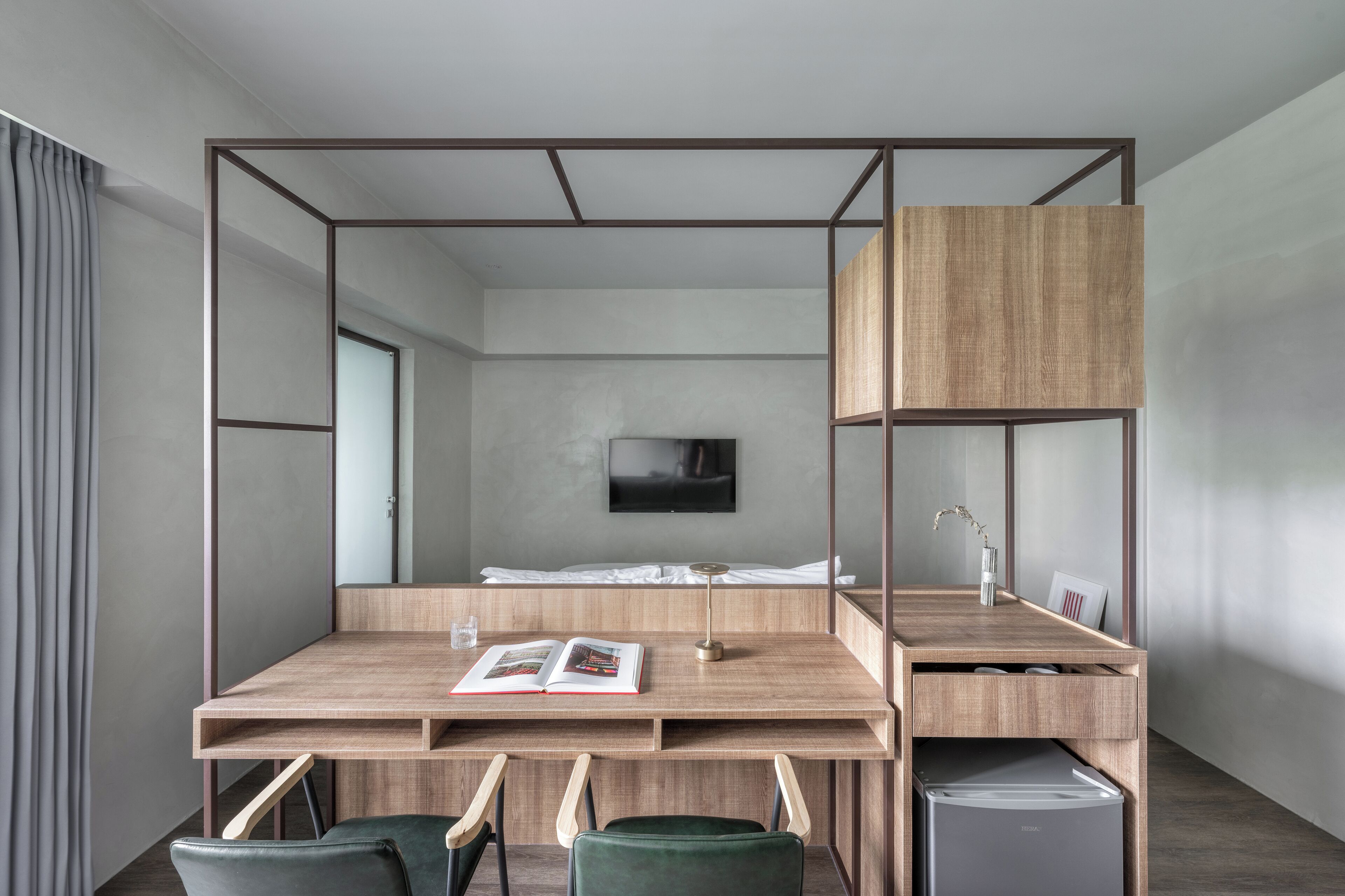A modern hotel room with a wooden desk, two chairs, a bed, a TV, and a small cabinet.