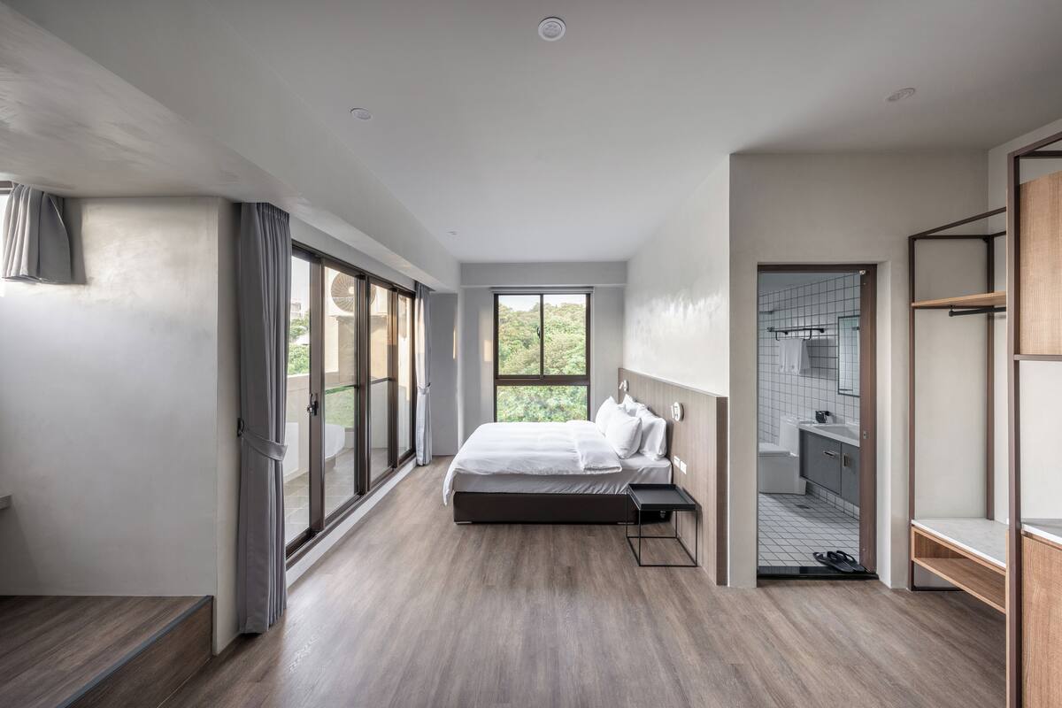 A modern bedroom with a large bed, a walk-in closet, and a bathroom visible through an open door.