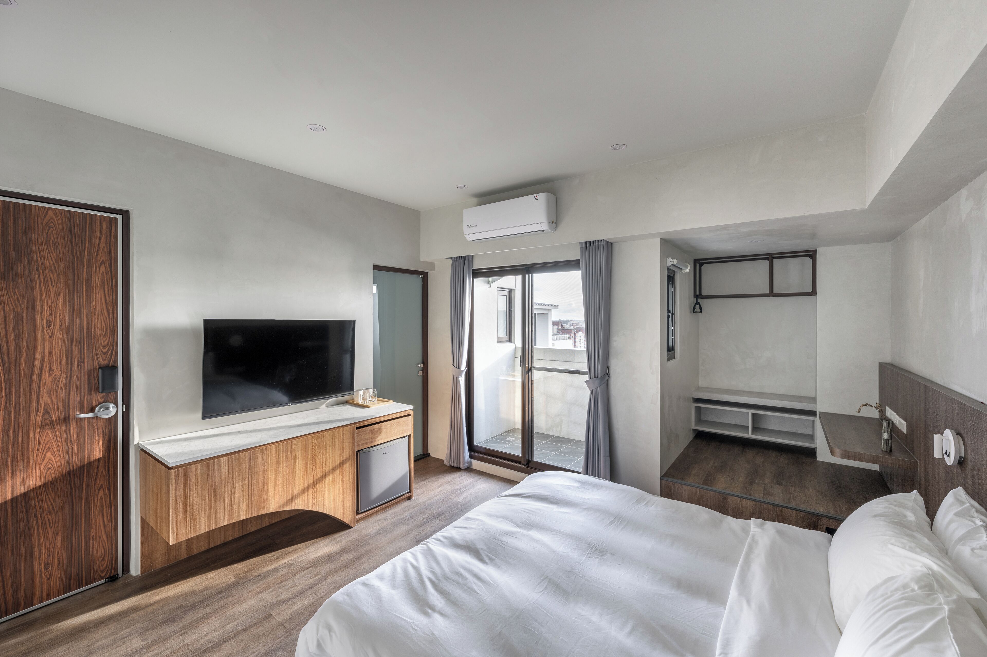 A modern hotel room with a large bed, a TV, a wooden desk, and a balcony with a view.