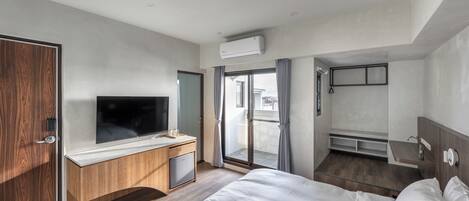 A modern hotel room with a large bed, a TV, a wooden desk, and a balcony with a view.