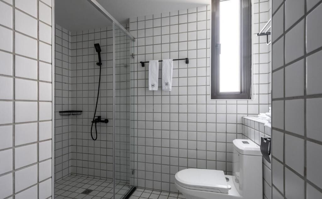 Un baño pequeño con azulejos, ducha, inodoro y ventana.