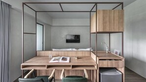 Una habitación moderna y minimalista con un escritorio de madera, dos sillas, un mueble pequeño y una cama con un televisor encima.