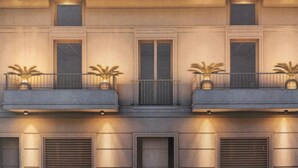 En bygnings facade med tre balkoner, hver med en lille plantekasse. Der er to vinduer på hver etage, og bygningen har et symmetrisk design med en muret dør i midten.