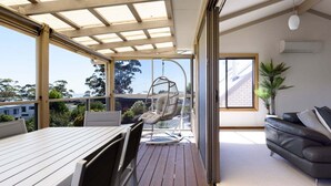 Un balcón moderno con mesa y sillas de madera, una silla colgante y un sofá.