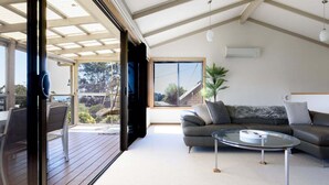 Una sala de estar moderna con una mesa de centro de vidrio, un sofá y vistas a un jardín a través de grandes ventanales.