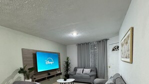 Una sala de estar moderna con un televisor de pantalla plana, sofás grises, una mesa de centro y una planta en maceta.