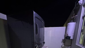 Un pequeño balcón con un mueble negro para televisor, un calentador de agua y una ventana.