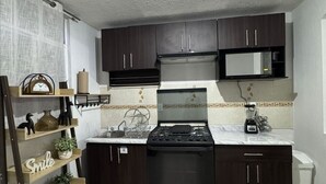 Una cocina compacta con armarios oscuros, una estufa a gas, un microondas y un lavamanos.
