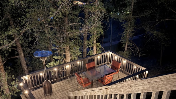 A wooden deck with a glass table and chairs, surrounded by trees. - The Little House on the Hill - Families Look Here (Divide)