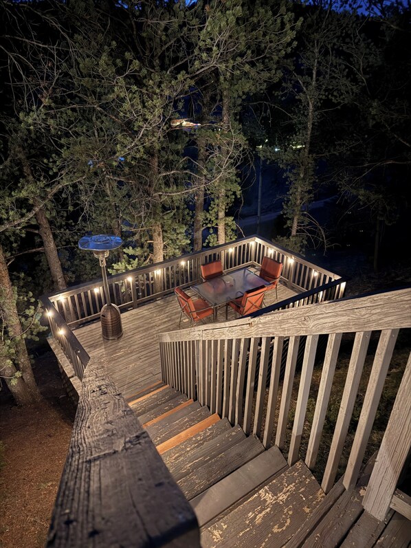 Eine Holzterrasse mit Glastisch und Stühlen, umgeben von Bäumen.