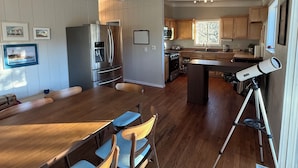 A spacious kitchen with wooden cabinets, a dining area with a long table and chairs, and a telescope on a tripod. - The Little House on the Hill - Families Look Here (Divide)